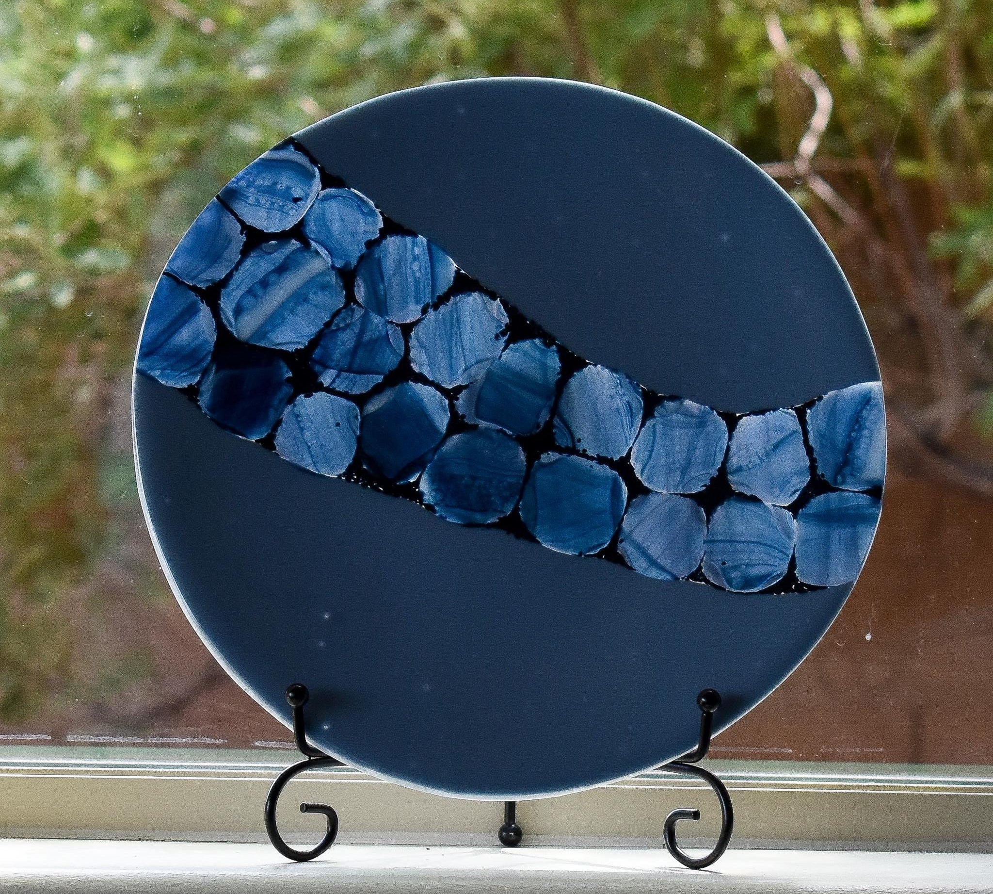 Payne&#39;s gray fused glass plate with sparkling blue accent path on stand in window