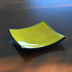 Six inch square fused glass tray with sloped corners. Yellow in center, trimmed and backed with black.