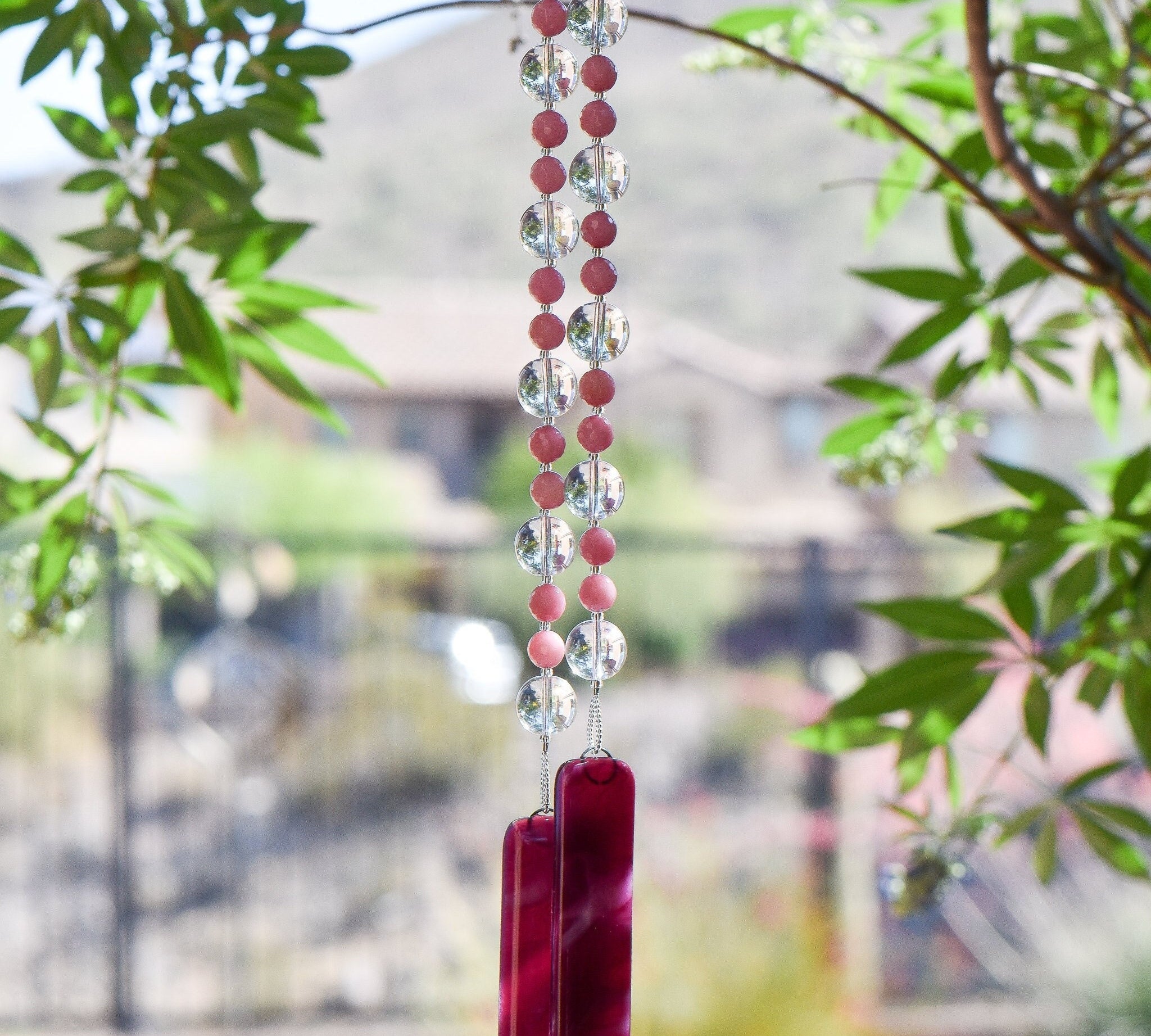 Light pink gemstone beads paired with large, clear glass beads, hanging vertically from tree, anchored by two pieces of cranberry pink fused glass.