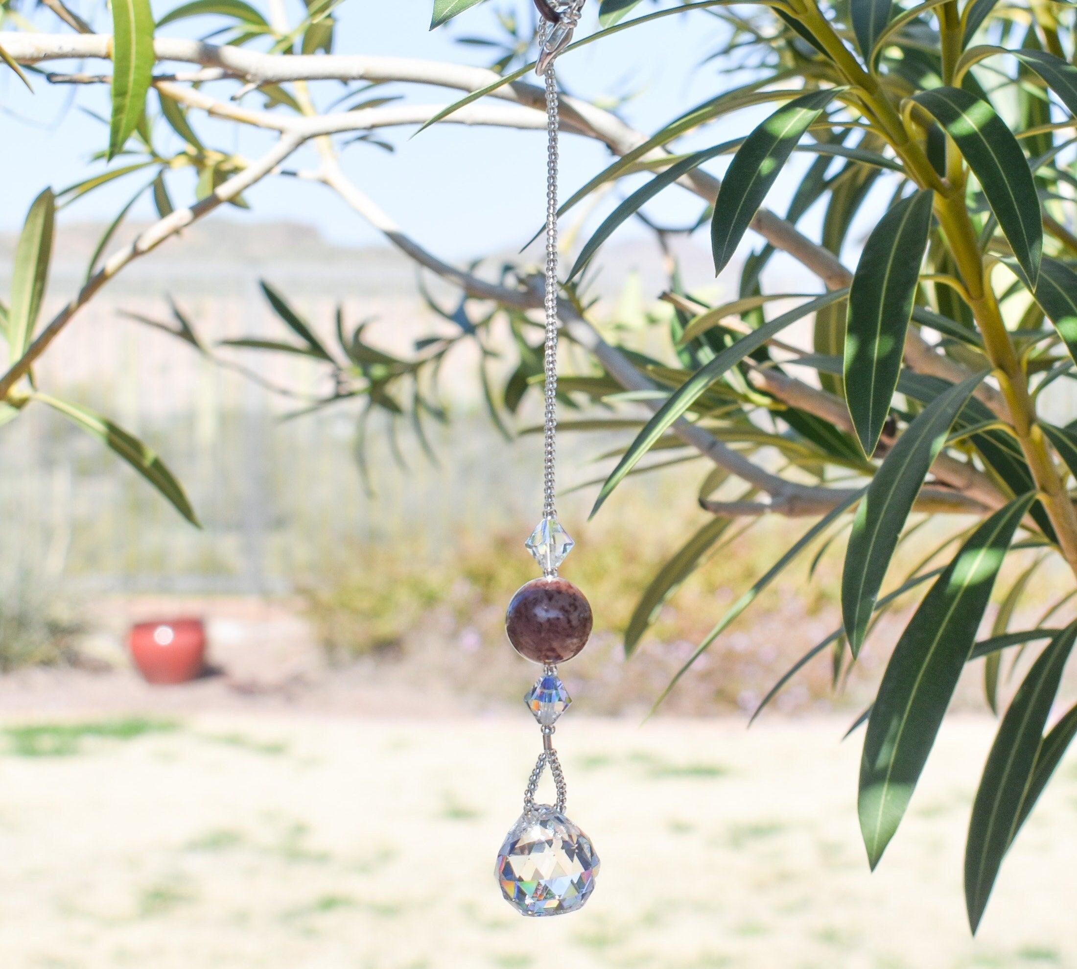 Round jasper stone strung with two bicone crystal beads and anchored by round crystal prism, hanging from tree