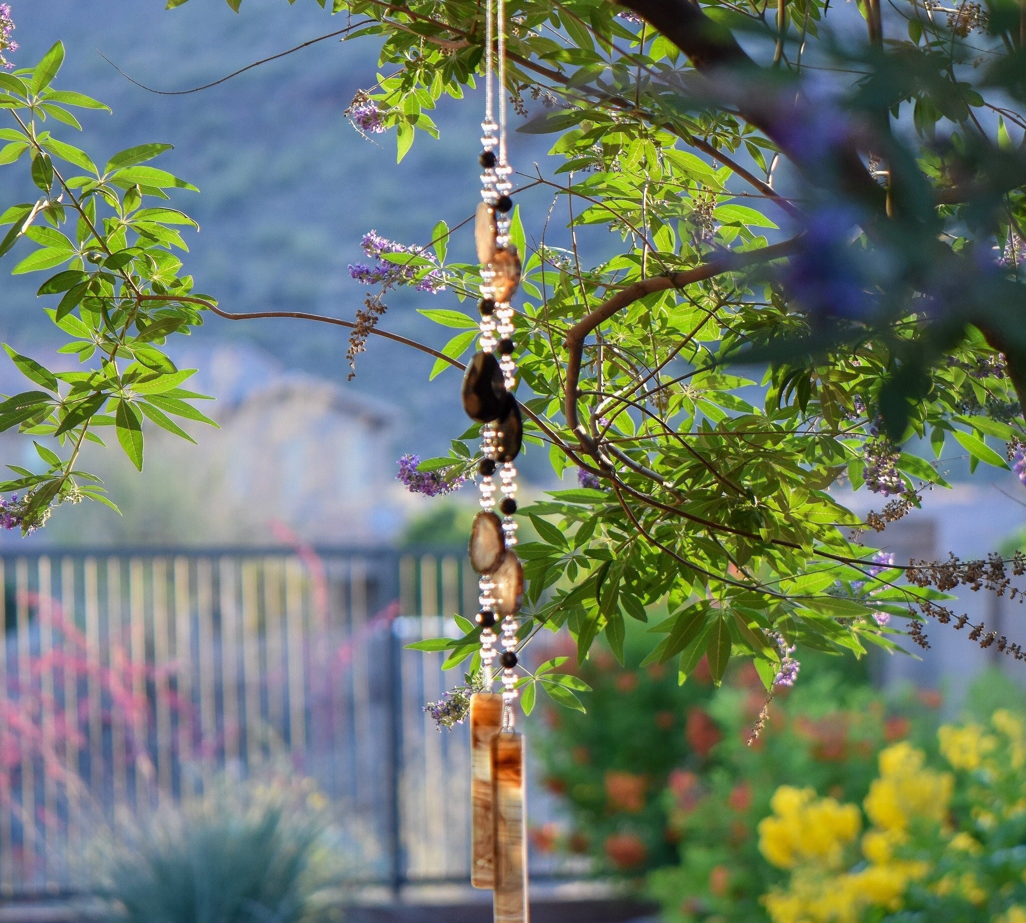 Large black agate slice beads and very large onyx beads strung with smaller clear and black onyx beads, hanging vertically from vitex tree with brown and black translucent fused glass anchors.