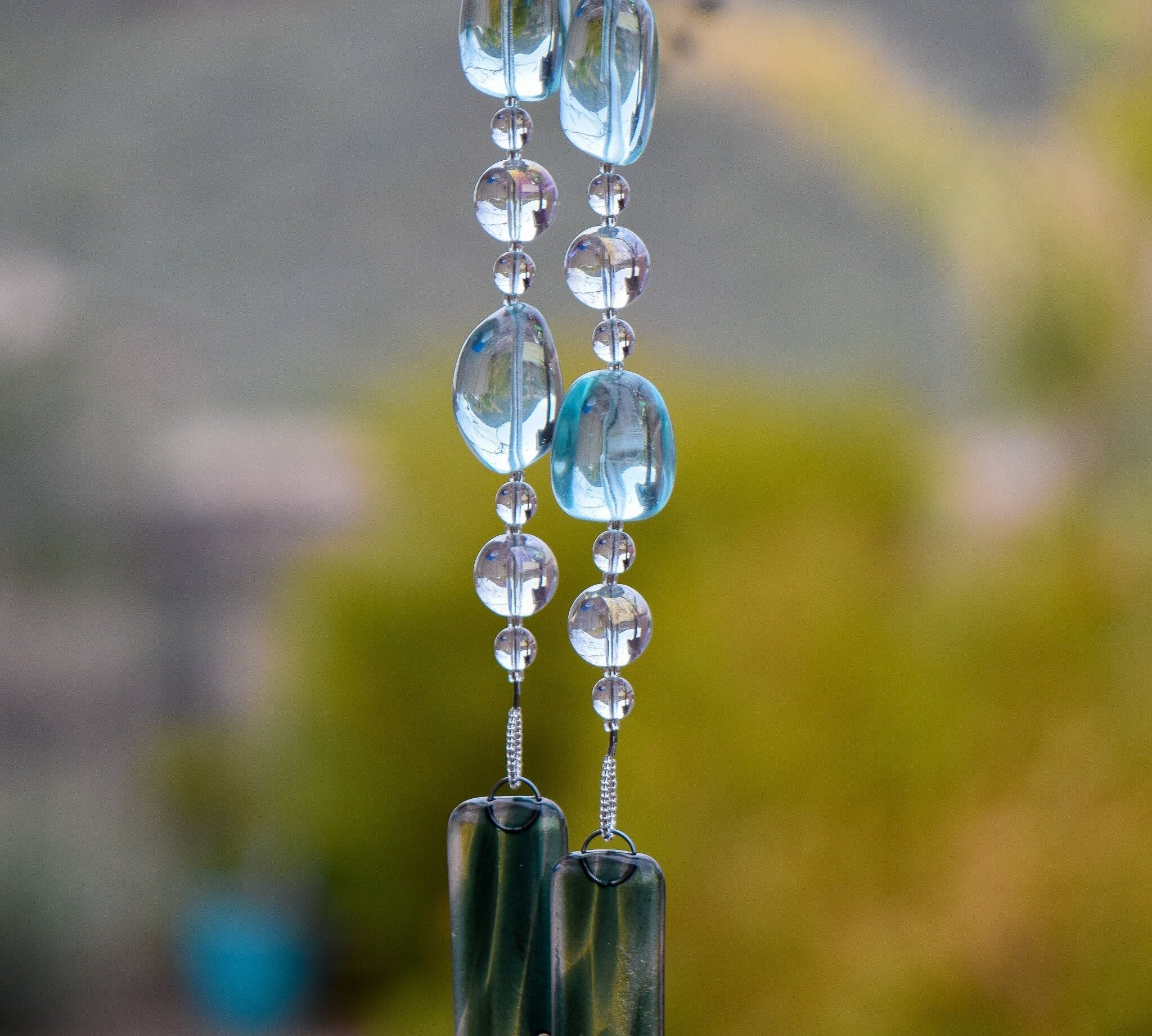 Very large solid glass aqua-colored beads paired with smaller clear glass beads, strung on wire and hanging vertically, anchored by two strips of sparkling green/aqua fused glass