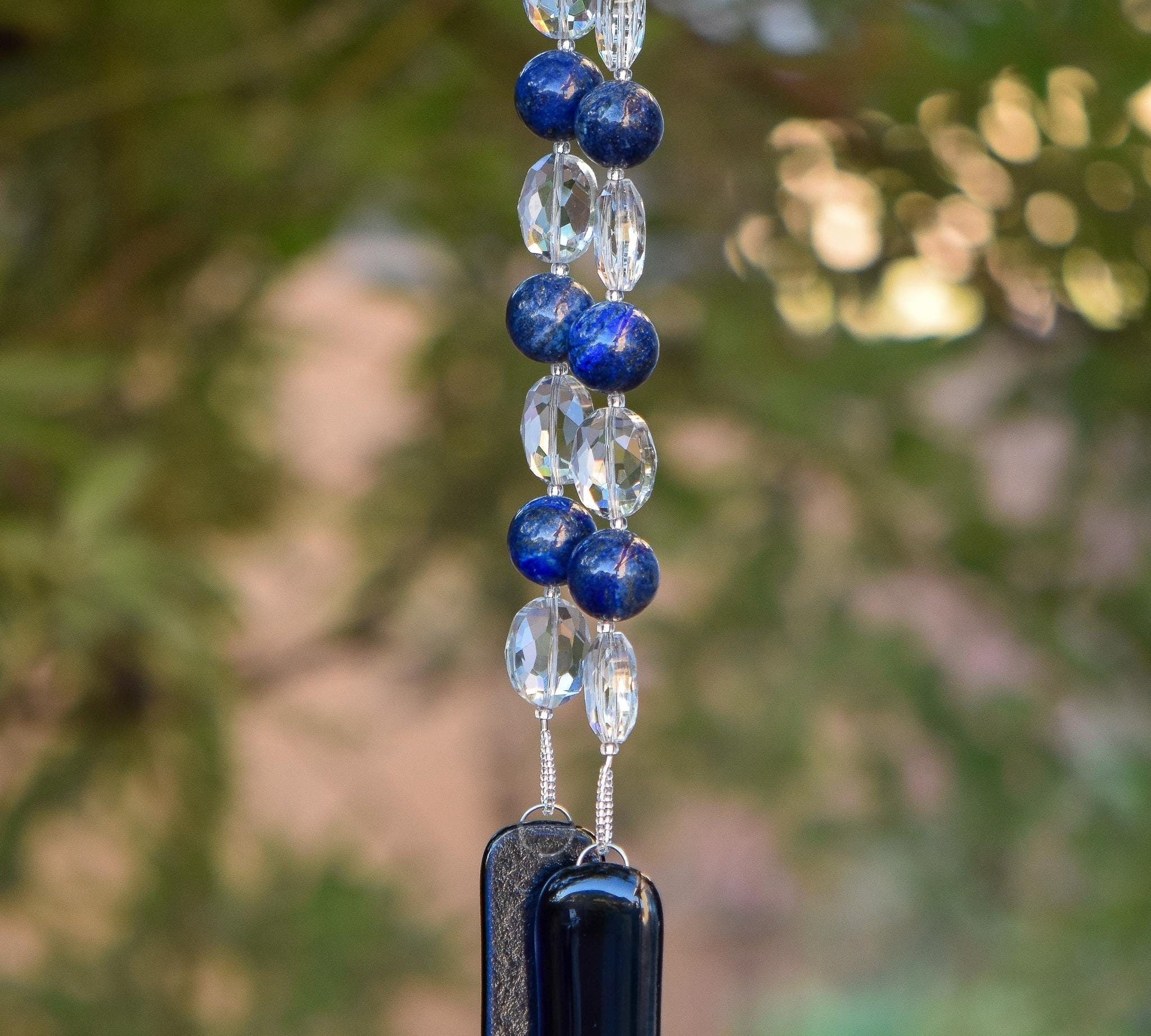 Large round blue lapis lazuli beads strung with crystal ovals, anchored by two pieces of navy blue fused glass, hanging from tree.