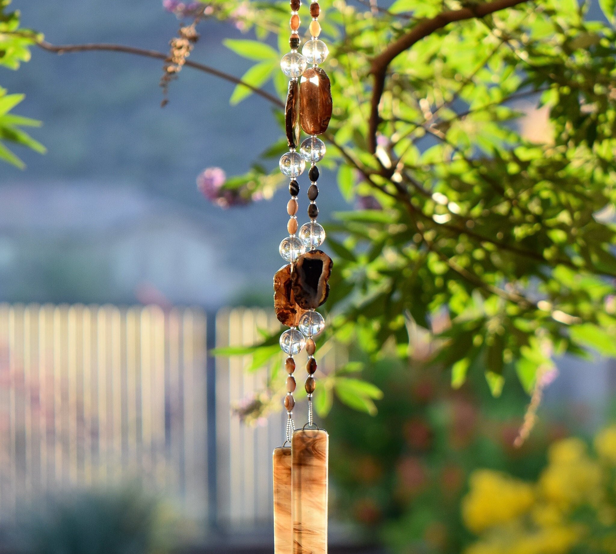 Two beaded wires hanging vertically from Vitex tree. Beads include large black agate slices, smaller agate tubular beads and large clear glass beads. Wire is anchored by two brown and white fused glass pieces.