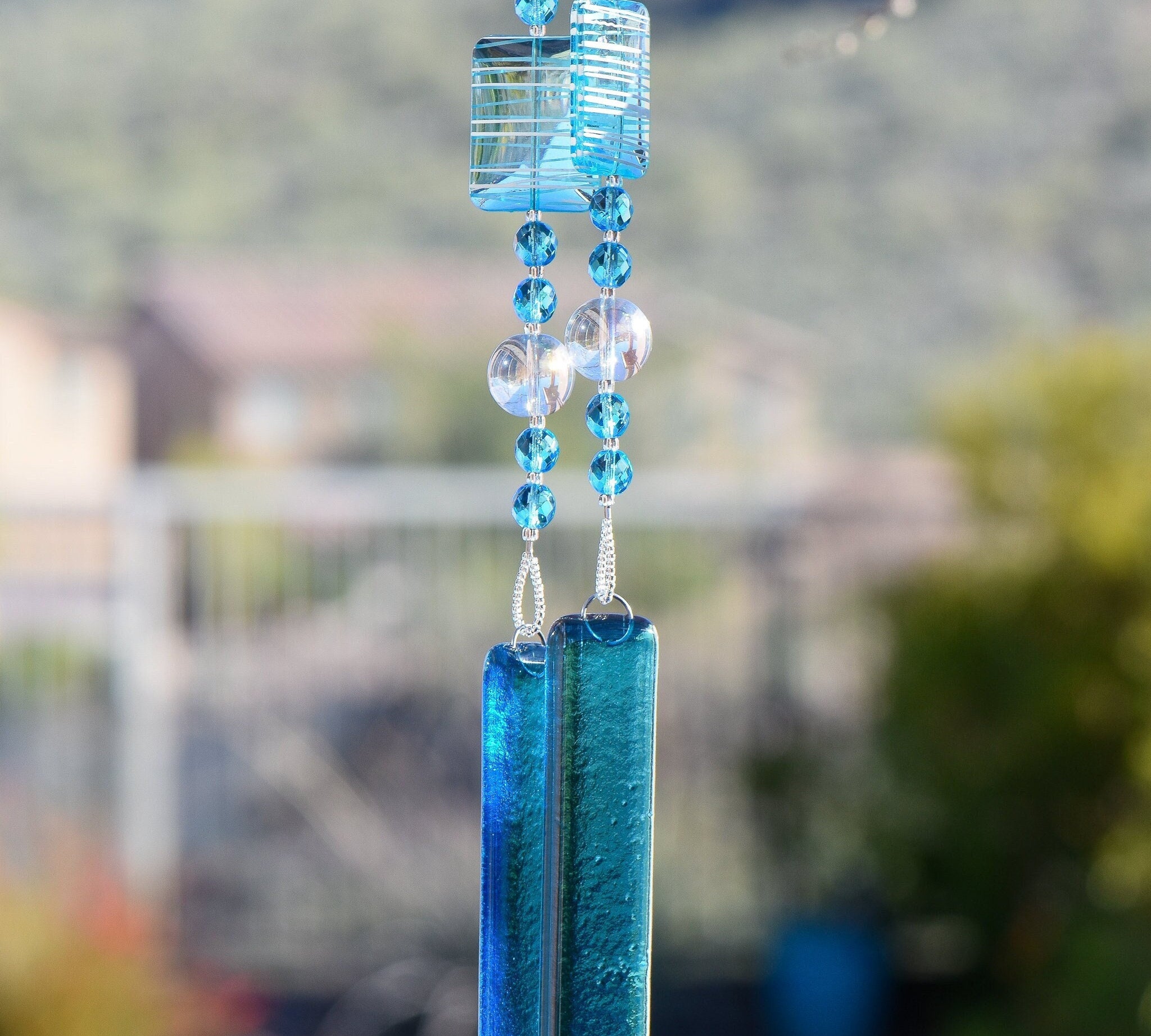 Large rectangular beads in sky blue with matching smaller round beads and large clear beads, all hanging vertically from a tree. Anchored by two pieces of sky blue fused glass