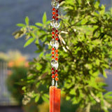 Small, round red agate stone beads paired with oval glass crystal beads, hanging vertically from tree, anchored by two pieces of fused glass in autumn flame