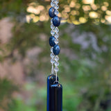 Oval dumortierite stone beads strung with clear glass crystal beads, hanging vertically from tree, anchored by two piece of transparent navy blue glass.