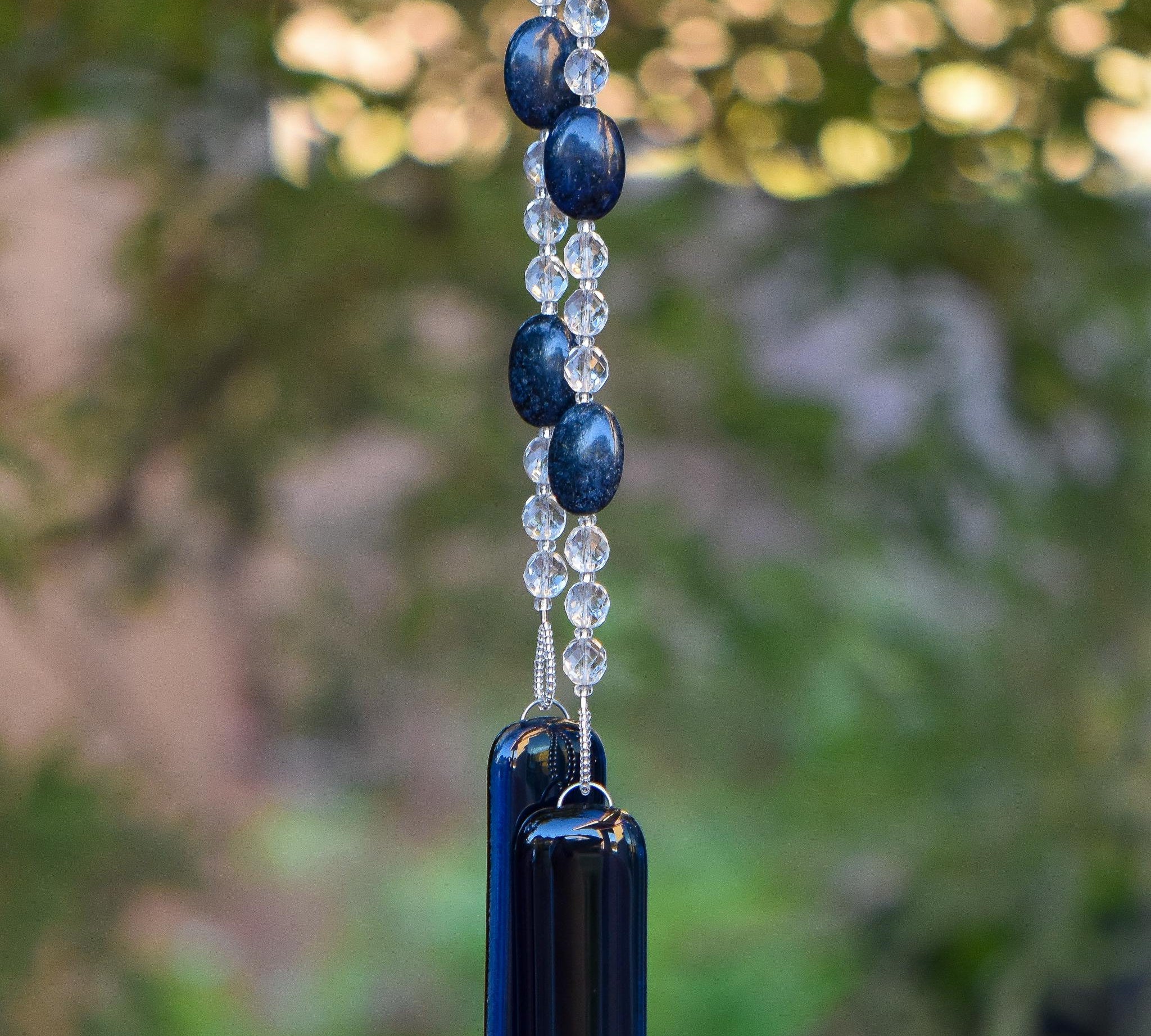 Oval dumortierite stone beads strung with clear glass crystal beads, hanging vertically from tree, anchored by two piece of transparent navy blue glass.