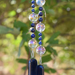 Large glass crystal beads strung with two sizes of small lapis lazuli stone beads, hanging vertically, anchored by two pieces of navy blue fused glass.