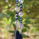 Large glass crystal beads strung with two sizes of small lapis lazuli stone beads, hanging vertically, anchored by two pieces of navy blue fused glass.