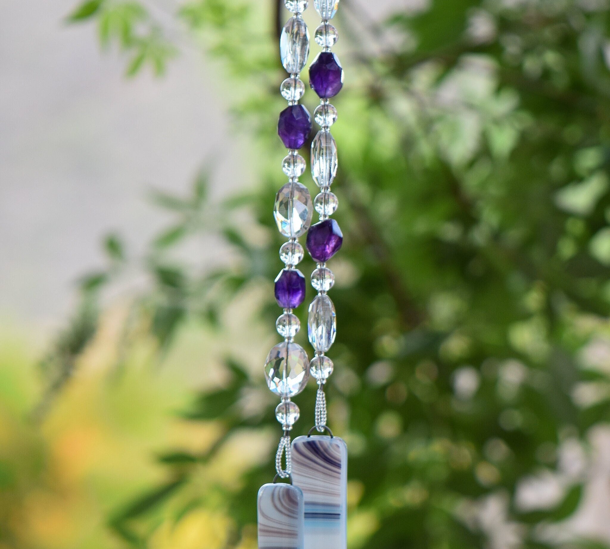 Amethyst stone beads paired with large crystal oval beads, clear glass beads, hanging vertically, anchored by two pieces of fused glass with purple/white/blue swirls.