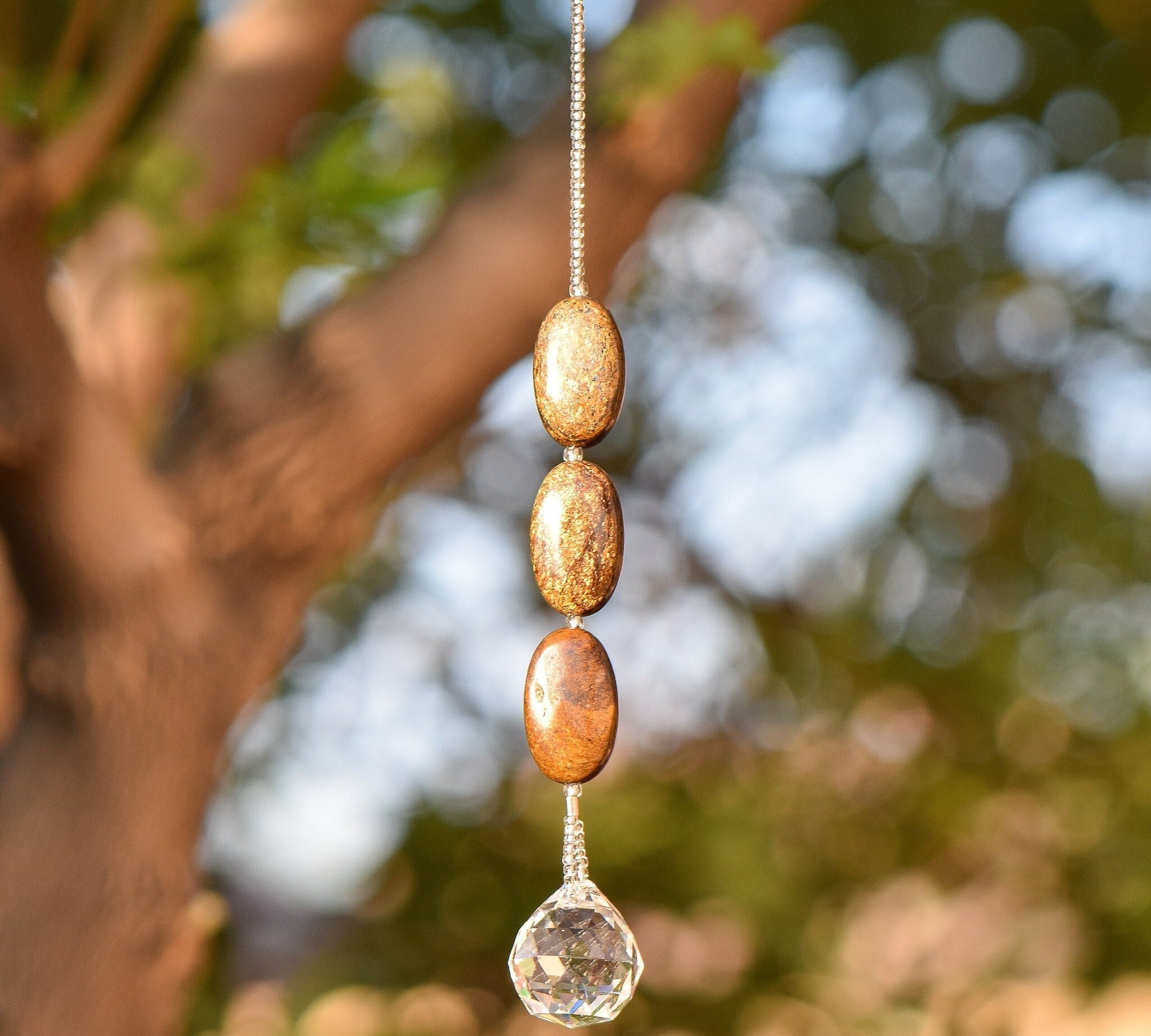 Three oval iron jasper stones strung on wire, hanging vertically, anchored by round crystal pendant.