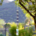 Purple pearl beads combined with large reflective glass crystal beads, strung on wire, hanging vertically, anchored by two pieces of fused glass with swirls of aqua, purple and white