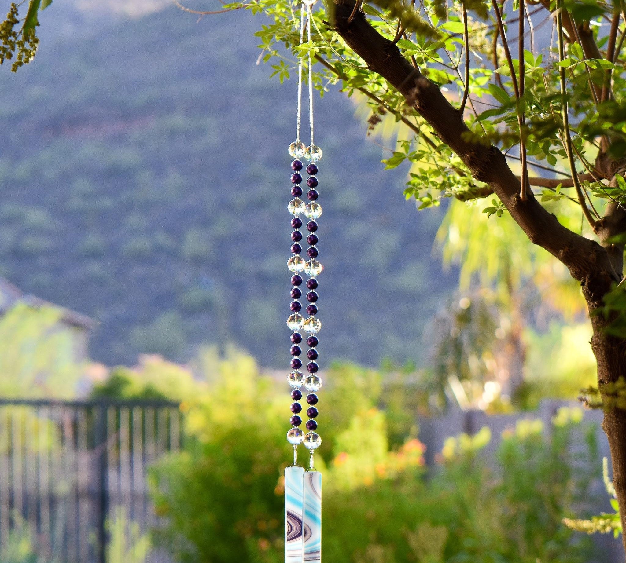 Purple pearl beads combined with large reflective glass crystal beads, strung on wire, hanging vertically, anchored by two pieces of fused glass with swirls of aqua, purple and white