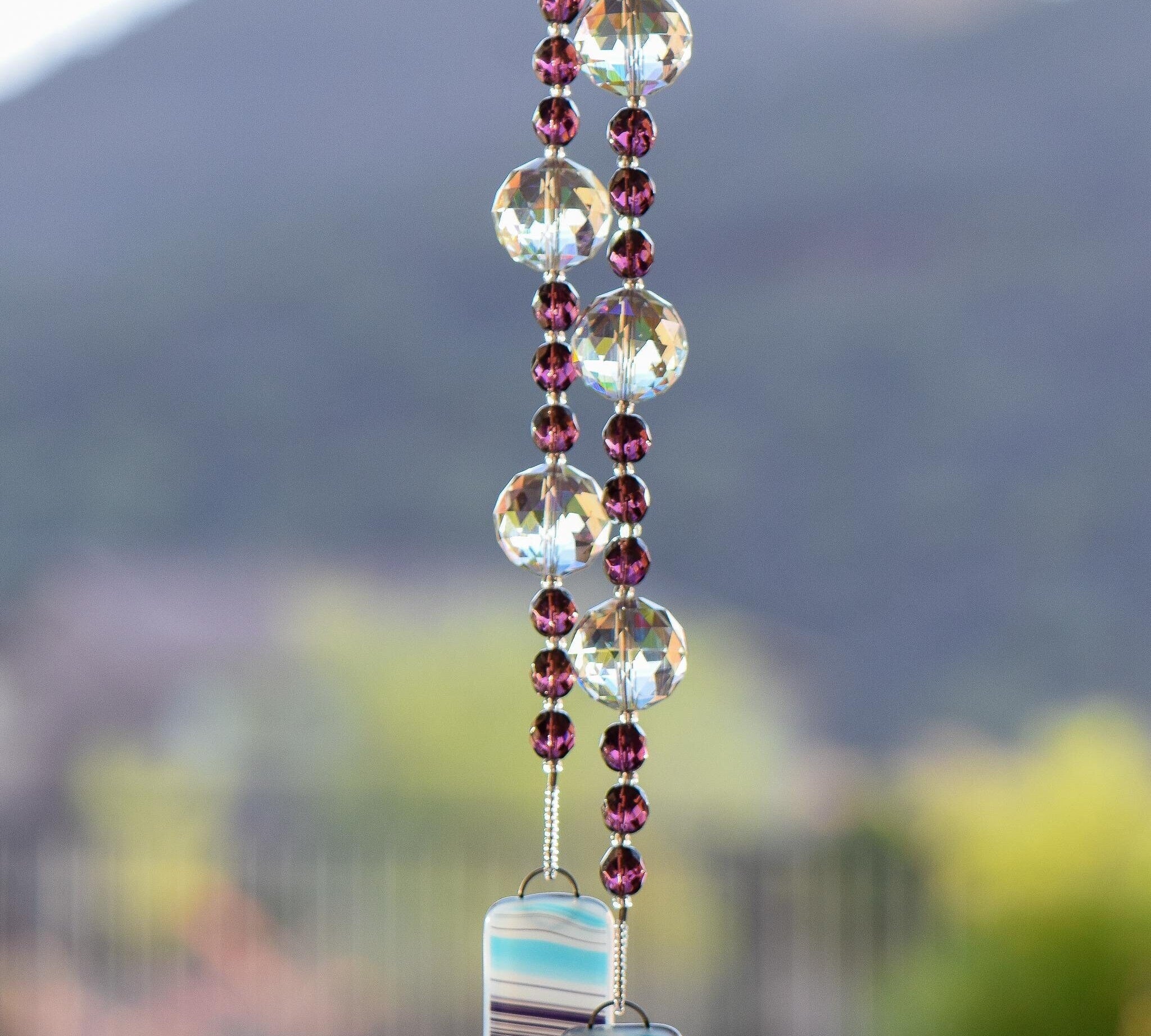 Faceted amethyst glass beads strung on wire with large glass crystal beads, hanging vertically, anchored by two pieces of kiln-formed swirled glass in aqua, purple and white