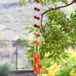 Large, round, faceted orange/red carnelian agate stones strung with glass beads, hanging from a tree, anchored by two pieces of orange, red and clear fused glass