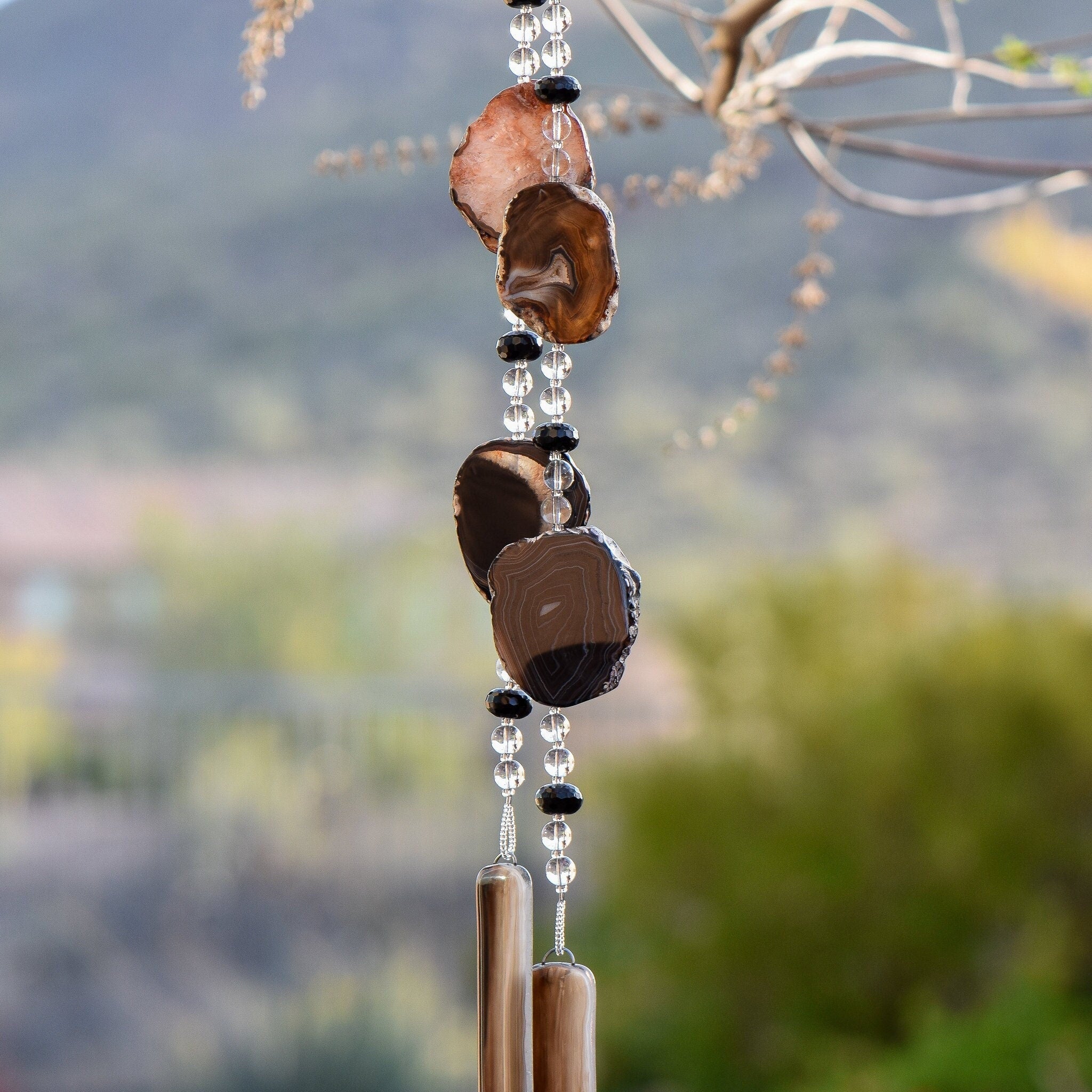 Large black agate geode slices strung with black onyx and clear glass, hanging vertically, anchored by two pieces of black and brown glass.