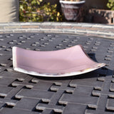 A light pink glass dish with a white rim. The dish is slightly curved and has a subtle sheen.