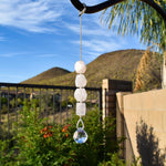 Four rose quartz stones strung vertically with a small round crystal prism at the bottom, in a suburban setting.