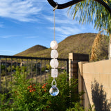 Four rose quartz stones strung vertically with a small round crystal prism at the bottom, in a suburban setting.