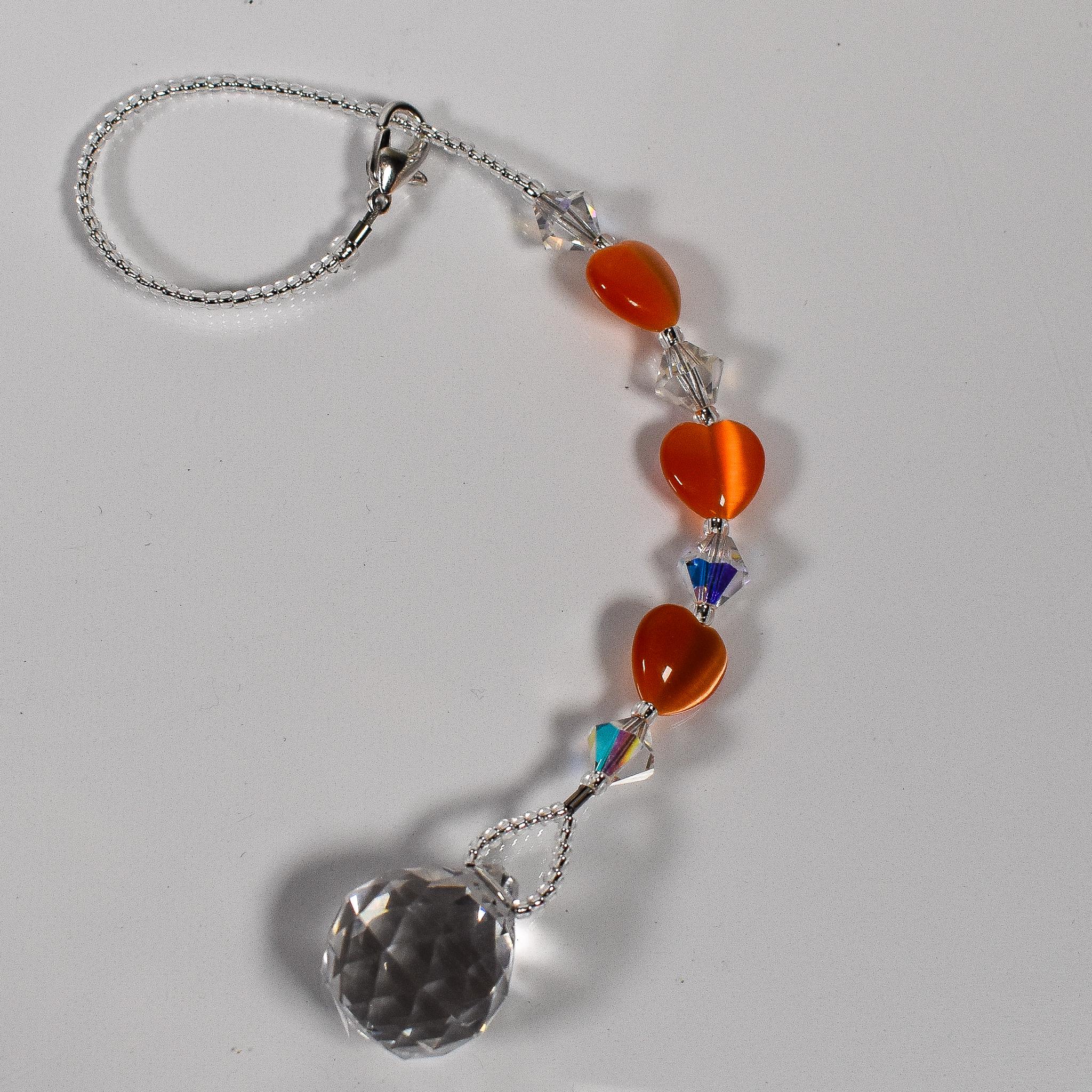 Small glass sun catcher made with small orange hearts, crystal bicones and a crystal prism, coiled up on white background.