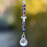 Crystal cross bead from Austria flanked by six Murano Glass beads in purple with silver foil, hanging vertically against blurred background, anchored by round glass crystal prism.