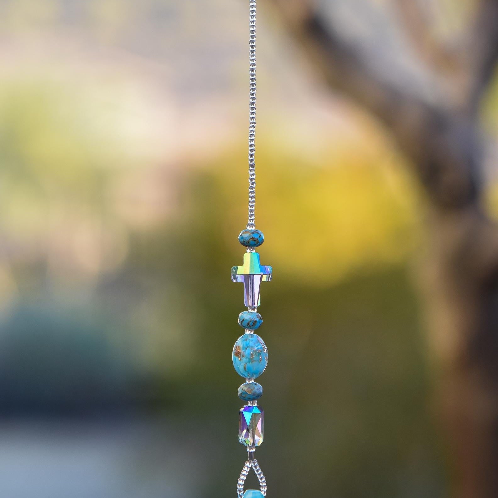 Glass turquoise-colored beads strung with a crystal cross, an emerald-cut crystal, hanging vertically, anchored by large aqua stone pendant.