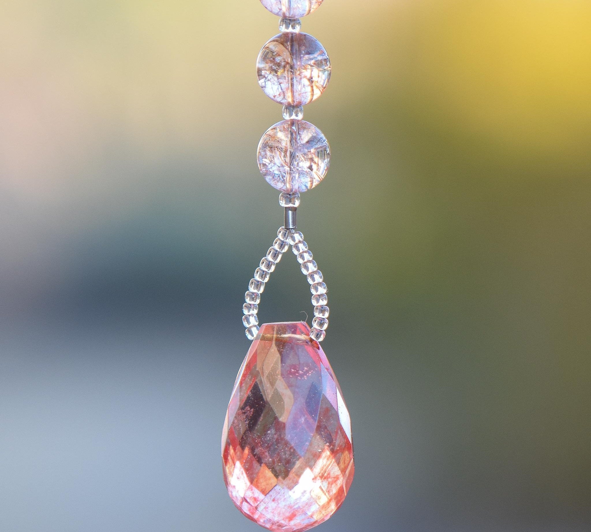 Large faceted pink stone pendant paired with crackle glass beads in a blush pink, hanging vertically in small sun catcher