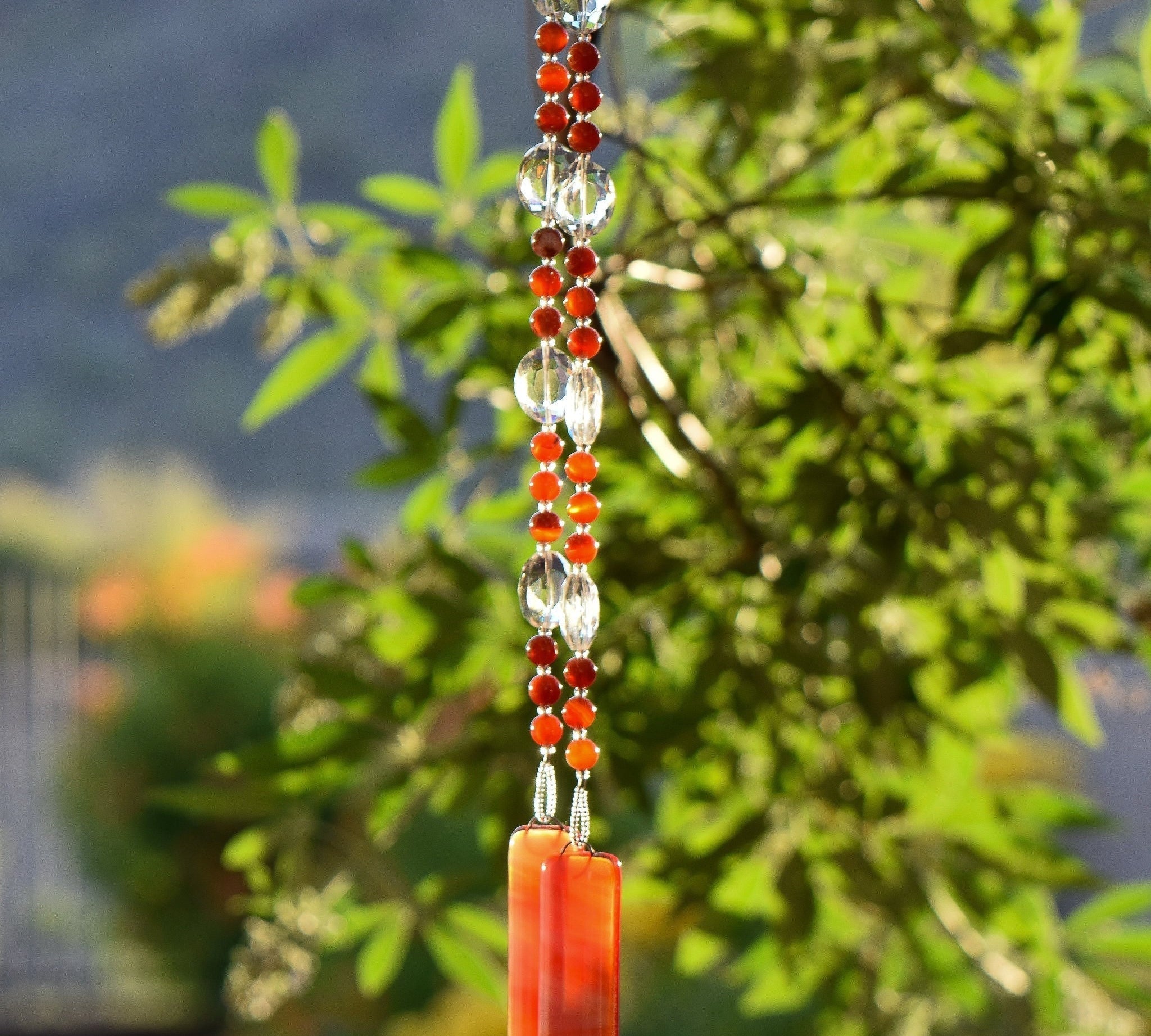 Small, round red agate stone beads paired with oval glass crystal beads, hanging vertically from tree, anchored by two pieces of fused glass in autumn flame