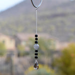 Small sun catcher hanging vertically in front of blurred background, made with six Murano glass cube beads flanking a large, round swirly bead and anchored by a large smoky quartz pendant