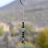 Small sun catcher hanging vertically in front of blurred background, made with six Murano glass cube beads flanking a large, round swirly bead and anchored by a large smoky quartz pendant