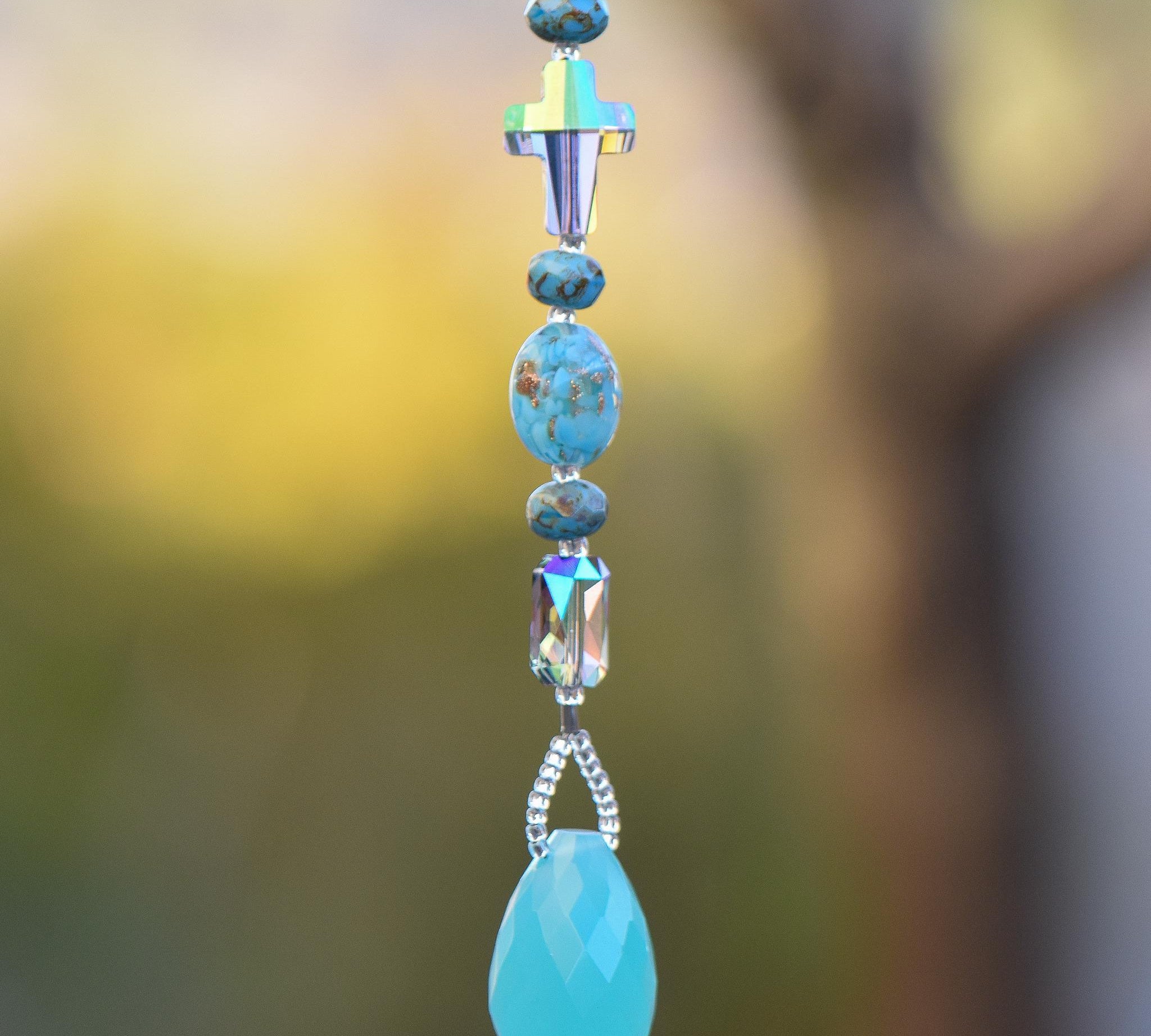 Glass turquoise-colored beads strung with a crystal cross, an emerald-cut crystal, hanging vertically, anchored by large aqua stone pendant.