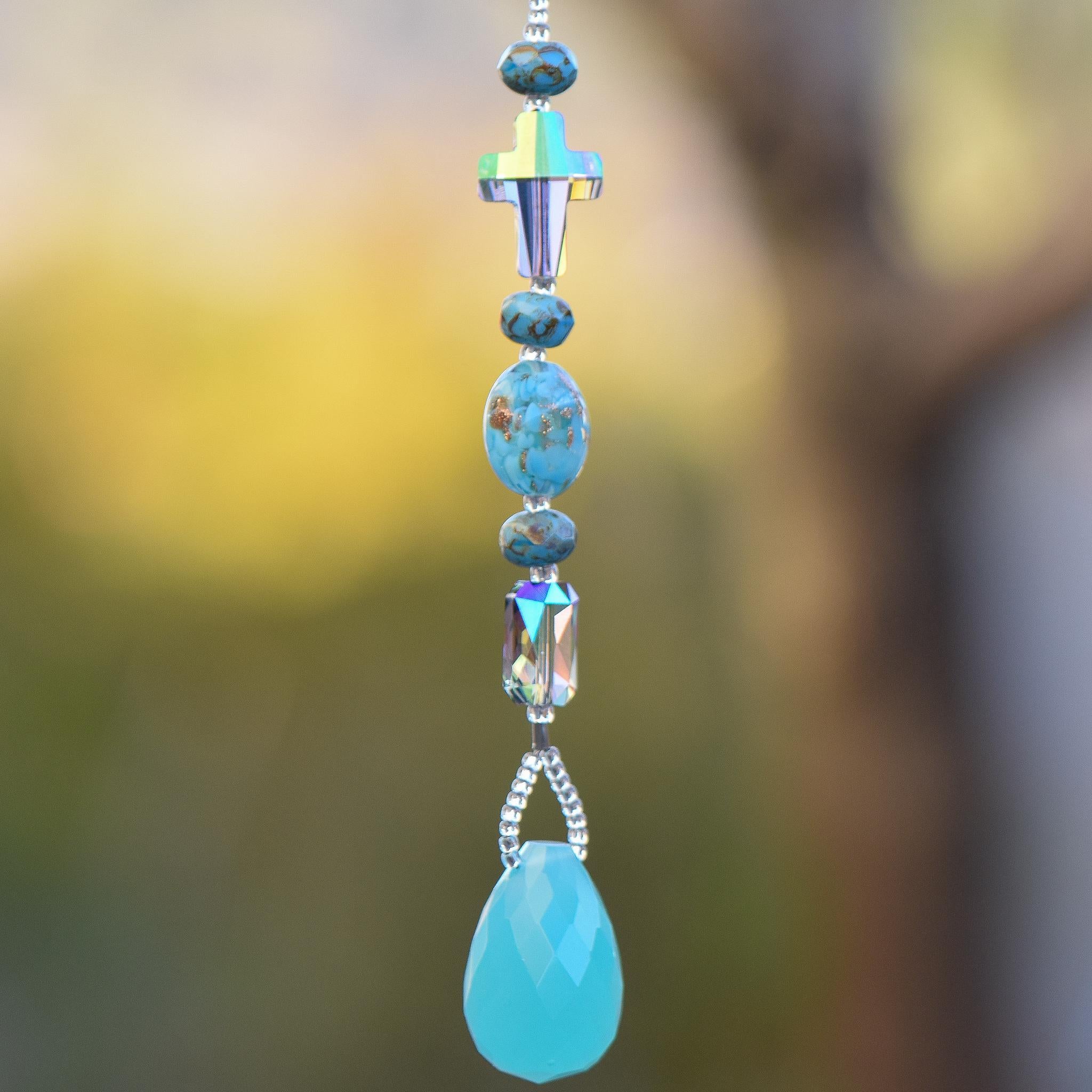 Glass turquoise-colored beads strung with a crystal cross, an emerald-cut crystal, hanging vertically, anchored by large aqua stone pendant.