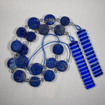Wind chime made with large thick lapis lazuli stone discs strung with glass beads coiled on flat white background.