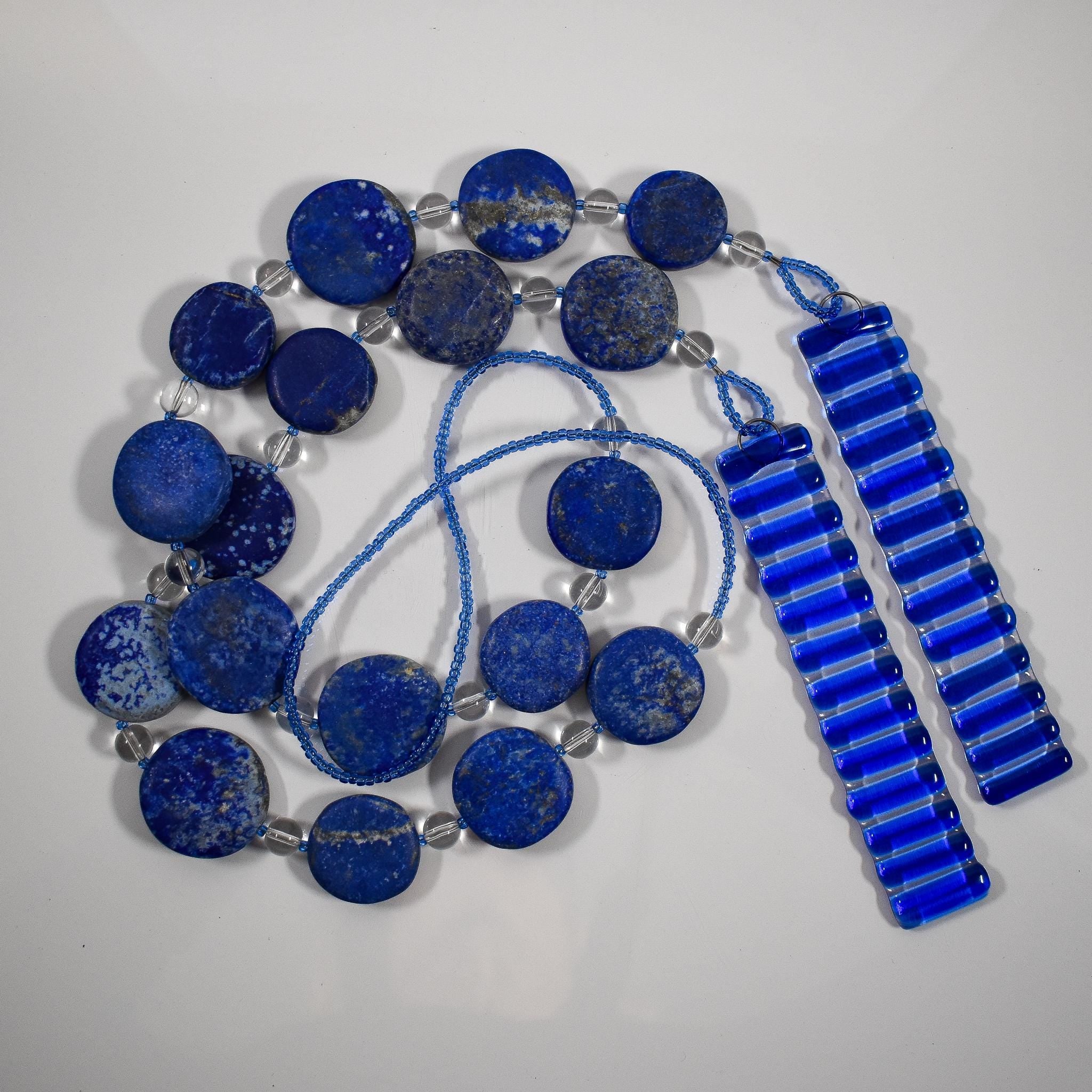 Wind chime made with large thick lapis lazuli stone discs strung with glass beads coiled on flat white background.