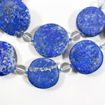 Large flat round lapis lazuli beads strung with smaller clear and blue glass beads, on white background.