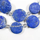 Large flat round lapis lazuli beads strung with smaller clear and blue glass beads, on white background.