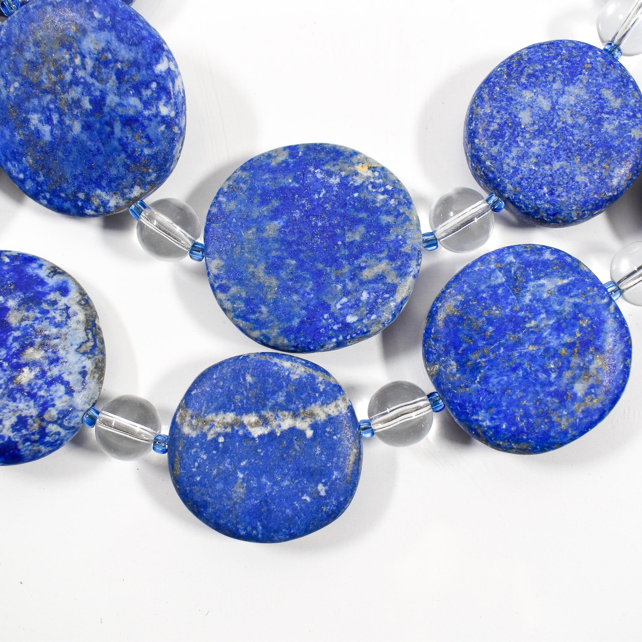 Large flat round lapis lazuli beads strung with smaller clear and blue glass beads, on white background.