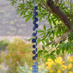 Hanging wind chime made with large thick lapis lazuli stone discs strung with glass beads, hanging vertically, anchored by two pieces of kiln formed clear glass with blue stripes.