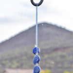 Wire covered in transparent blue seed beads, draped over shepherds hook against mountain background.