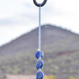 Wire covered in transparent blue seed beads, draped over shepherds hook against mountain background.