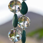 Three large glass crystal beads strung with teardrop-shaped magnesite stone beads, hanging vertically, zoomed in.