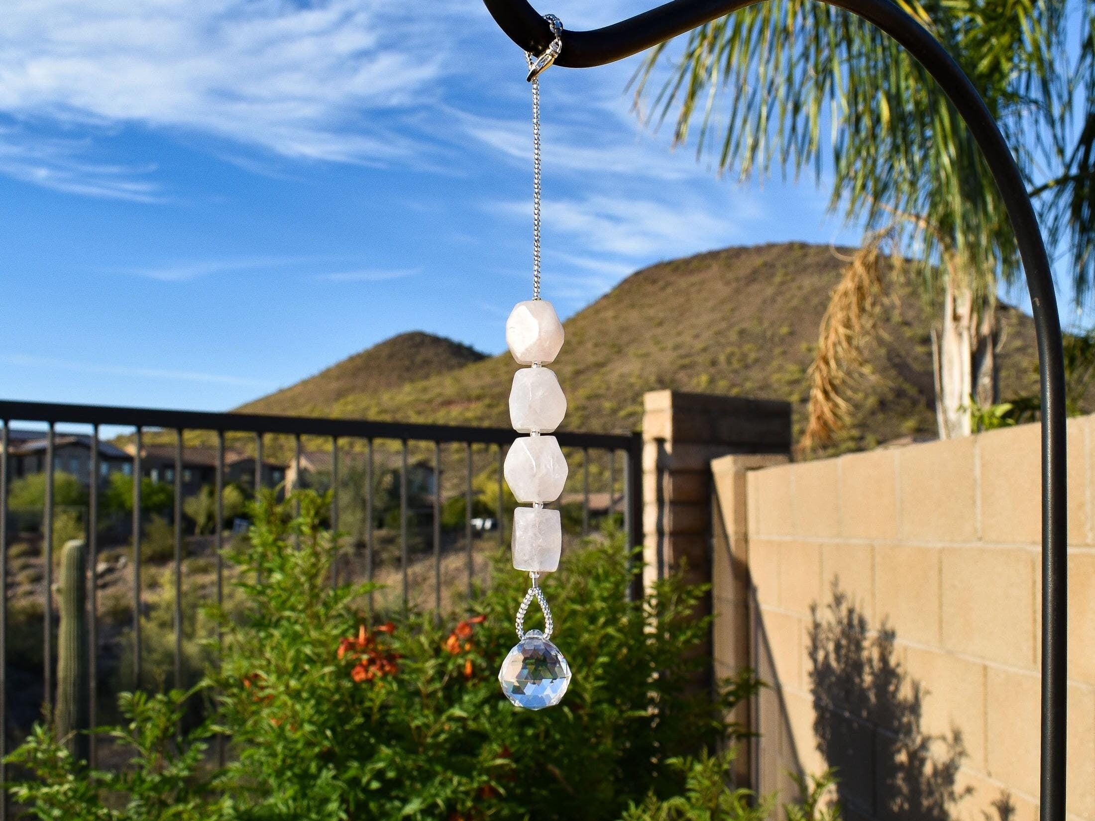 Four rose quartz stones strung vertically with a small round crystal prism at the bottom, against mountain background.