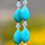 Four teardrop-shaped stone beads strung and hanging vertically with small bicone glass crystal beads. Blurred background.