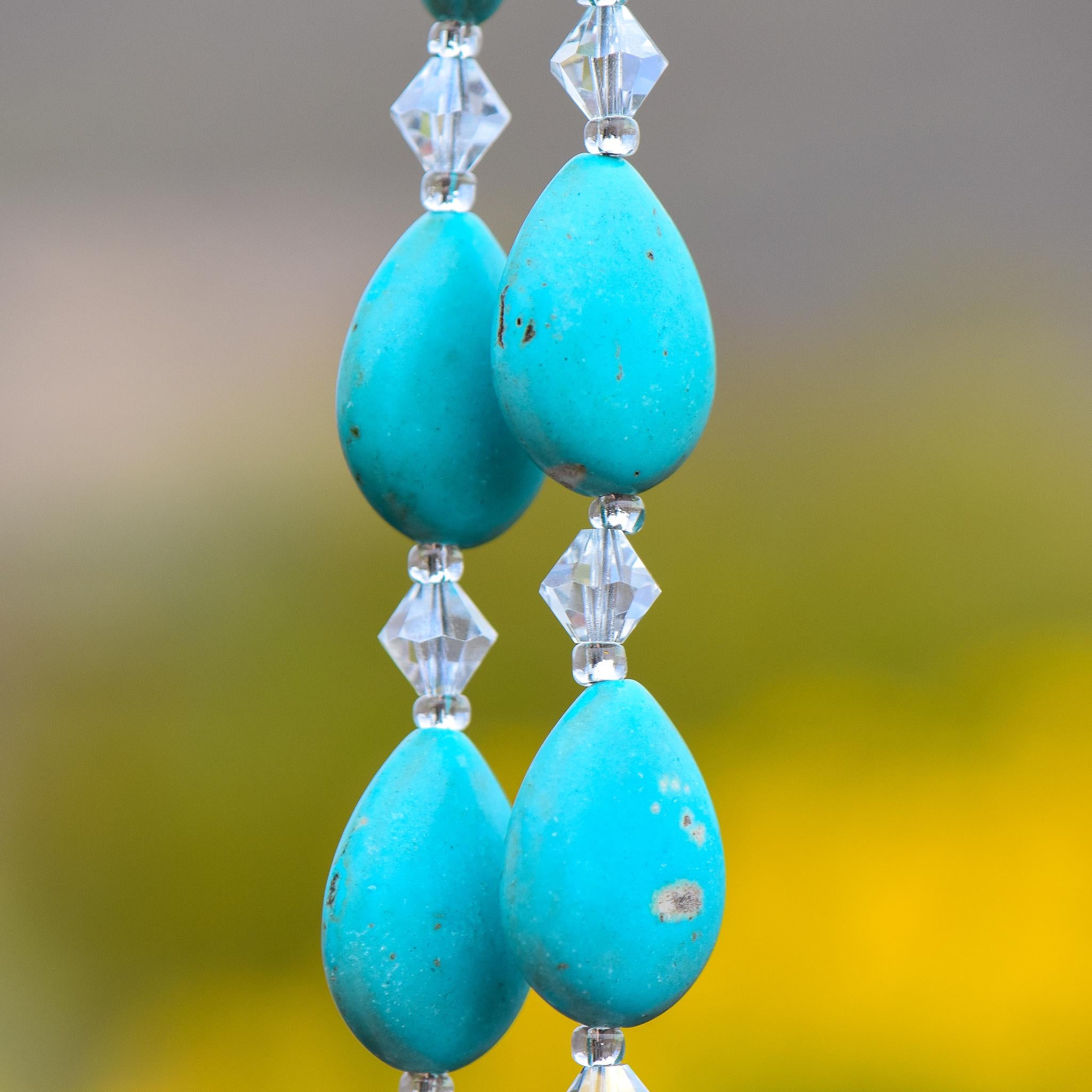 Four teardrop-shaped stone beads strung and hanging vertically with small bicone glass crystal beads. Blurred background.