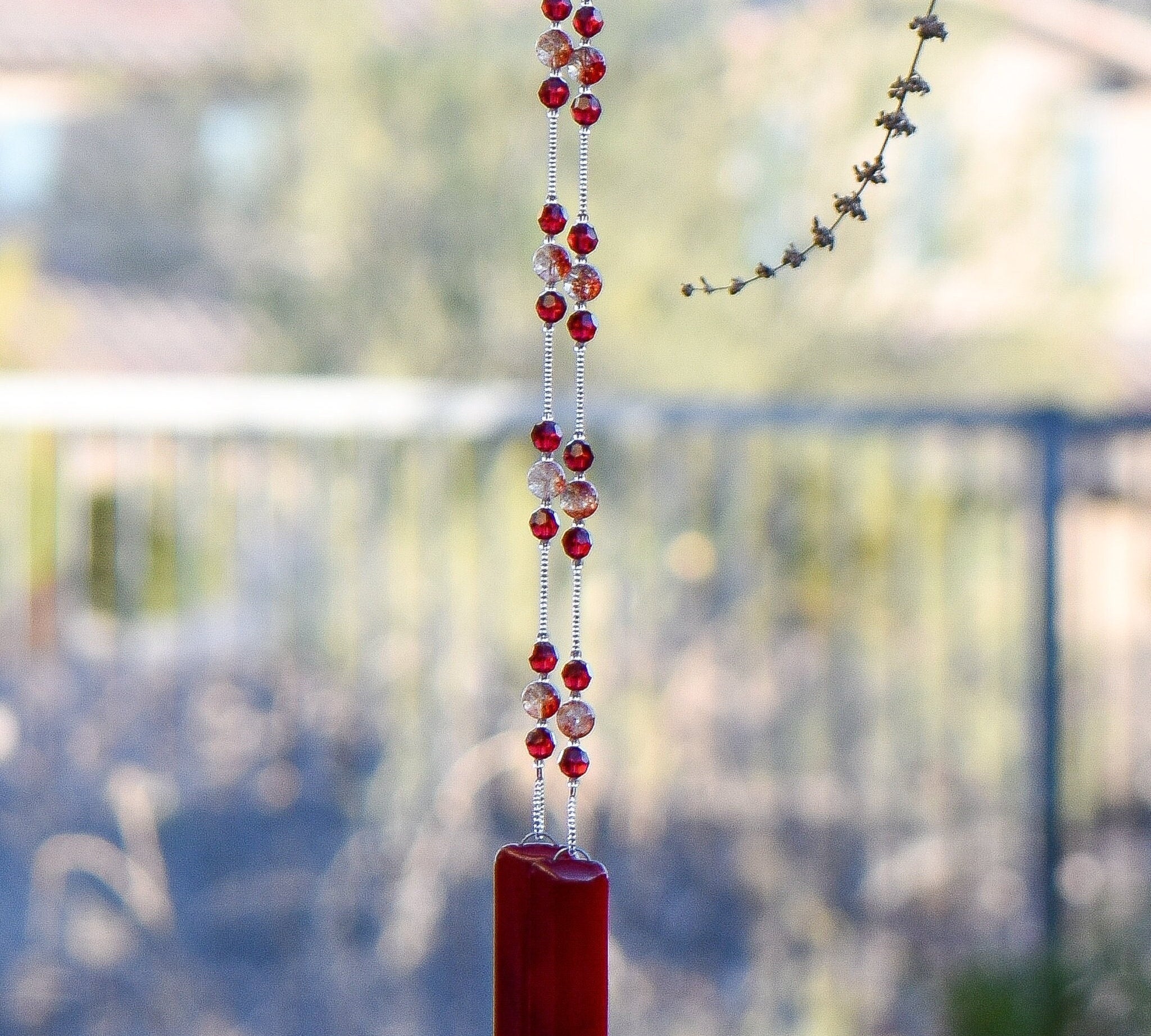 Handmade wind chime made with Red Ruby Moss Crystal stones flanked by Austrian crystal beads, anchored by two pieces of red fused glass, hanging from tree