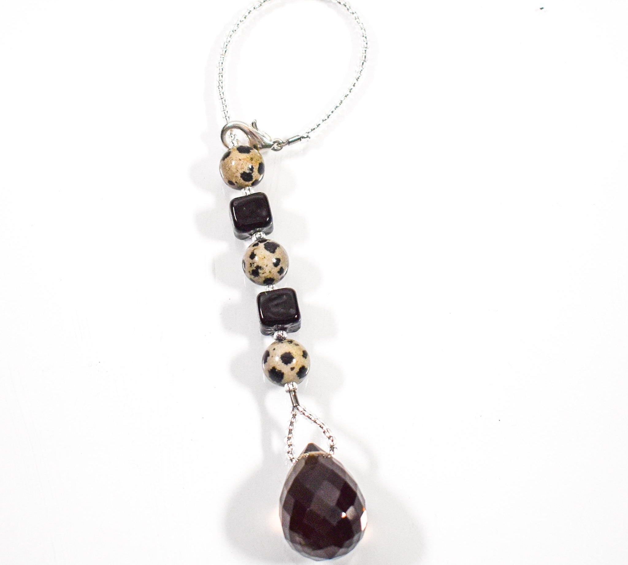 Small beaded sun catcher made with two black cube beads, three round tan beads with black spots and a large smoky quartz faceted tear drop pendant, hanging vertically against white background.