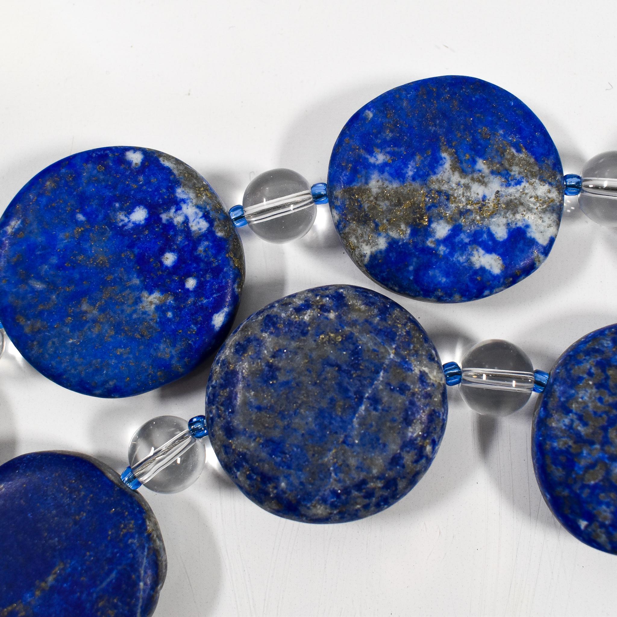 Large flat round lapis lazuli beads strung with smaller clear and blue glass beads, on white background.