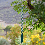 Turquoise Magnesite stone beads are teardrop-shaped and strung with large round clear glass crystal beads with lots of facets. All are hanging vertically against a mountain background, anchored by two pieces of kiln formed glass that is vanilla cream colored with a strip of peacock green.