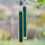 Two pieces of kiln formed glass hanging from wire in a tree. Each piece is rectangular shaped with a base of vanilla cream color and a strip of peacock green.